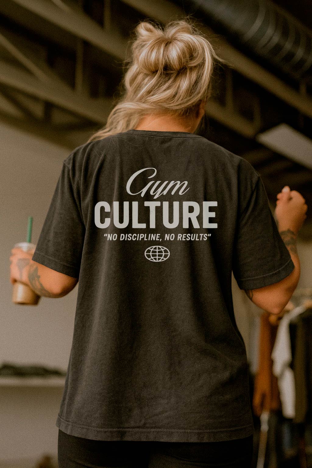 Black gym culture t-shirt with fitness motivation text worn by a woman in a gym setting