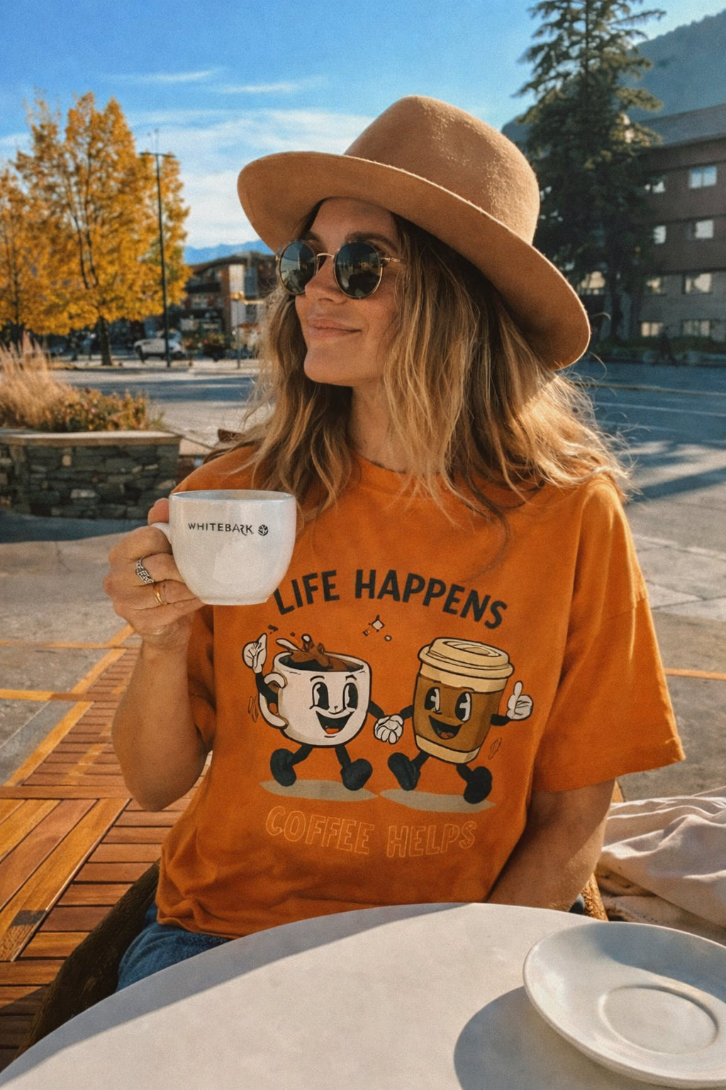 Woman in autumn cafe wearing orange Life Happens Coffee Helps graphic t-shirt
