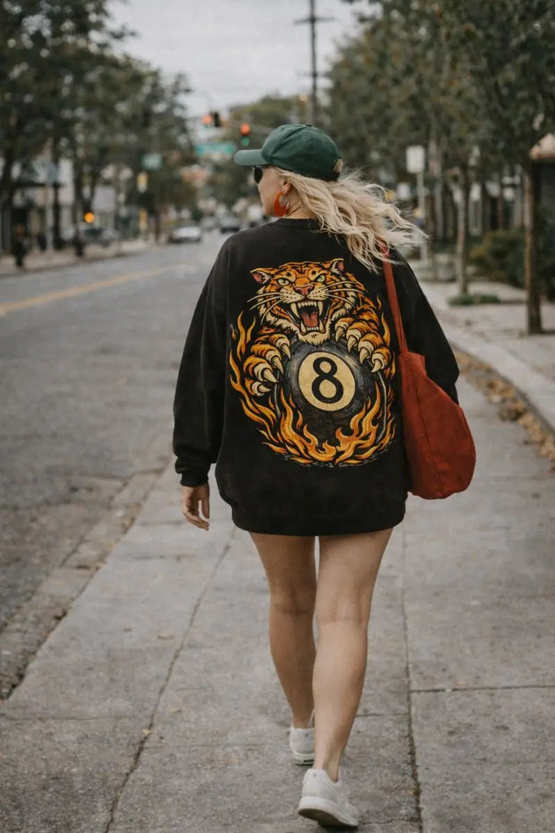 Full body lifestyle shot of retro graphic crewneck sweatshirt with vintage tiger 8 ball back print, worn oversized paired with sneakers and red tote bag