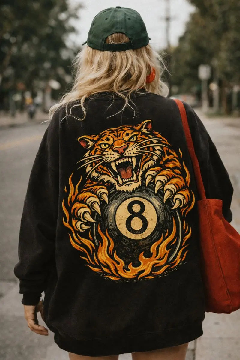 Woman wearing a black retro graphic sweatshirt with oversized vintage tiger and 8 ball back print, street style outfit with green cap and red bag