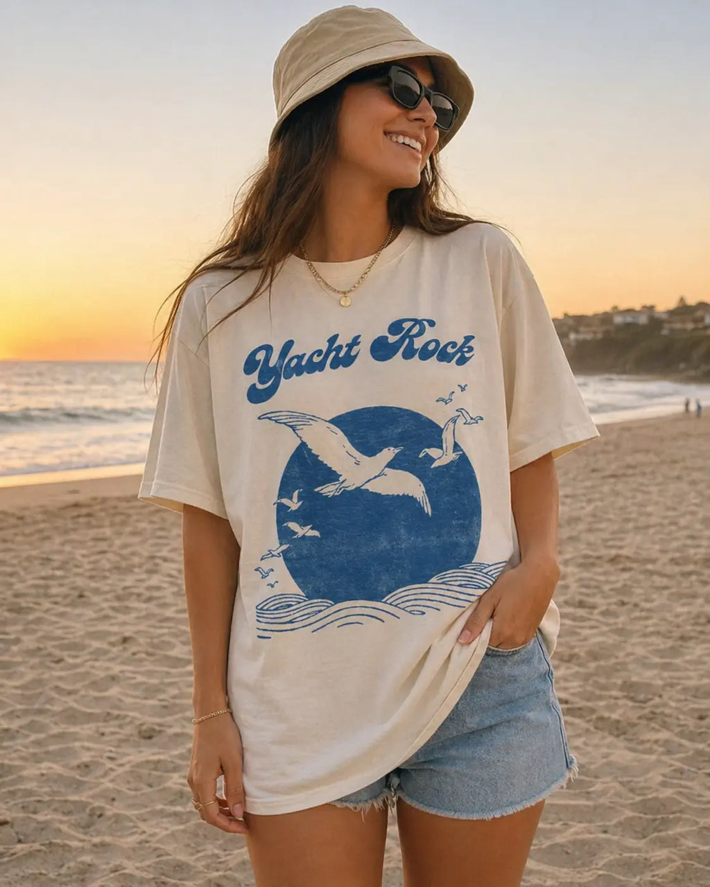 Woman wearing Yacht Rock vintage graphic tee in white at beach sunset — coastal graphic t-shirt for women