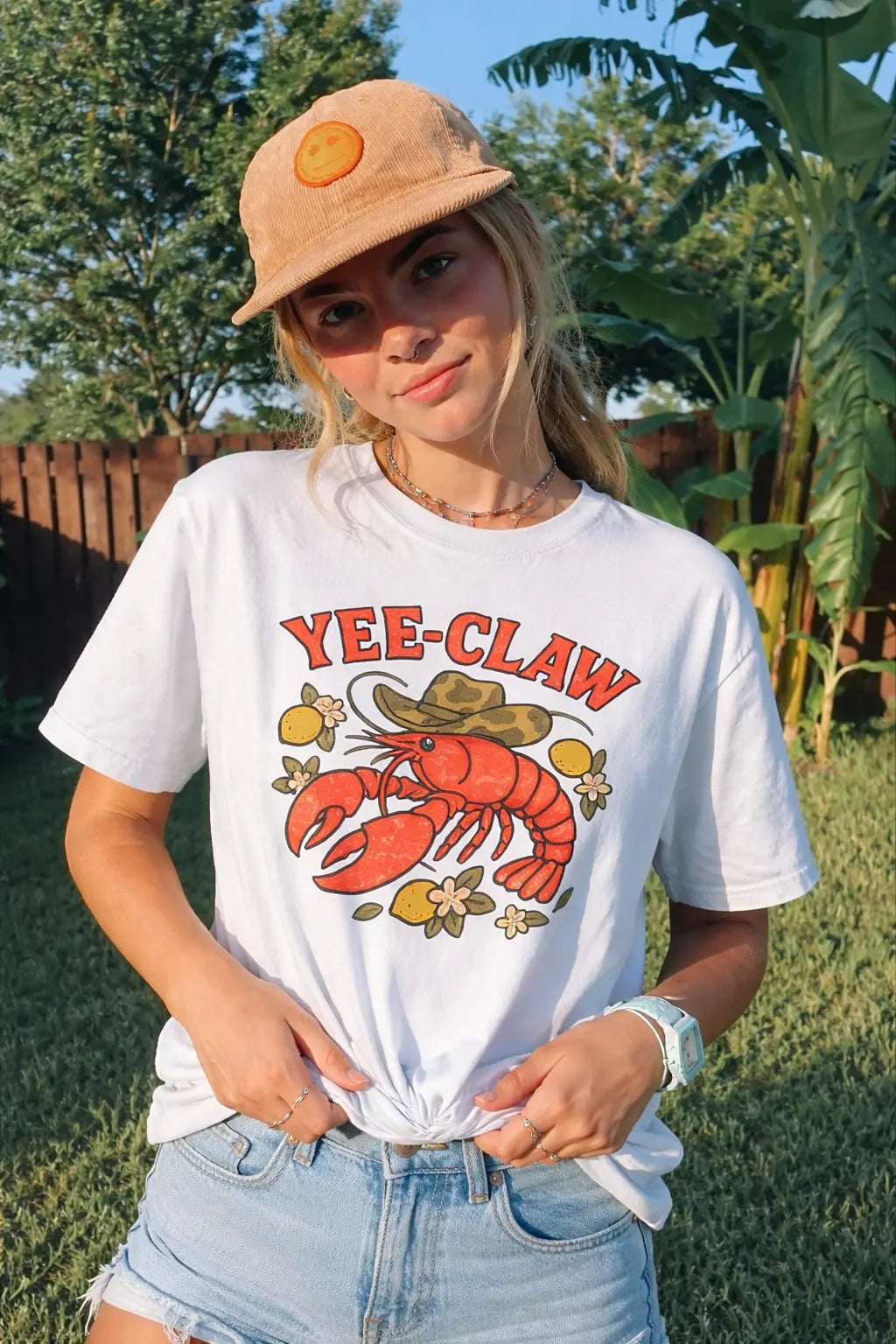Woman wearing a Yee Claw lobster graphic T-shirt styled casually outdoors in a garden setting